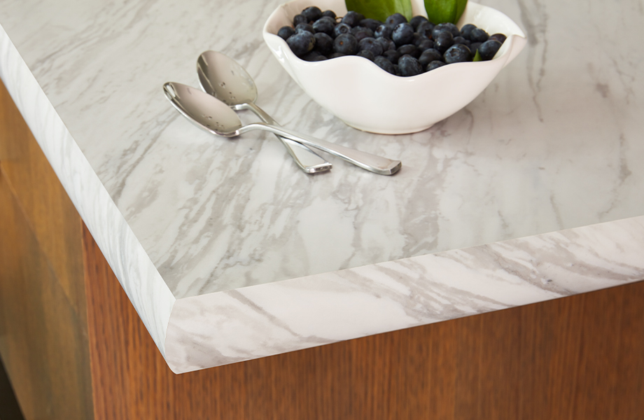 Edge of kitchen island with white marbled Formica laminate countertop, spoons and bowl of blueberries